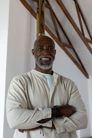 Confident senior african man standing arms crossed in minimalist loft wearing beige shirt