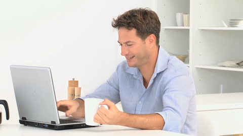 Man Enjoying Coffee While Chatting on Laptop in Kitchen