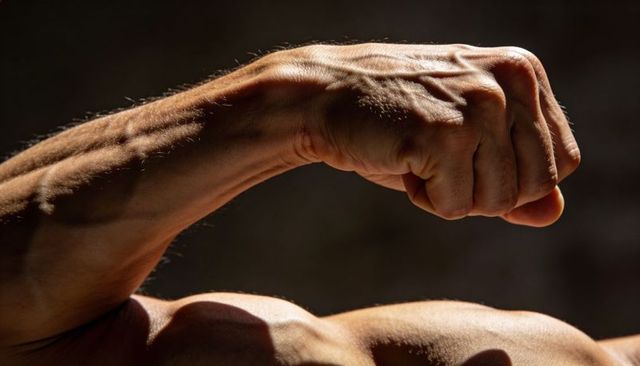 Vascular muscular male arm flexing with clenched fist closeup high-contrast texture