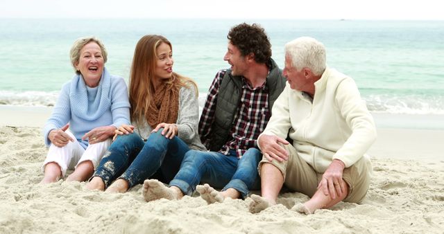 A cheerful multigenerational family sitting on sandy beach near ocean, smiling and talking. There are two older adults, likely grandparents, and a younger couple. Everyone is dressed casually for a day out. Use this image for advertising family vacations, retirement planning, travel blogs, or articles about family enjoyment and togetherness.