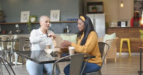 Two women sharing takeout and coffee in cozy urban cafe, catching up and enjoying friendship