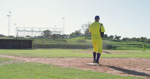 Pitcher standing on mound in bright yellow uniform and blue cap with sunlit green outfield