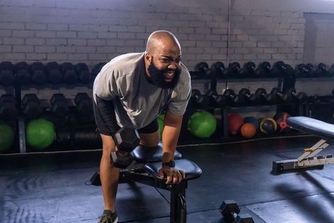African american man performing bent-over dumbbell row on bench in gym, strength training