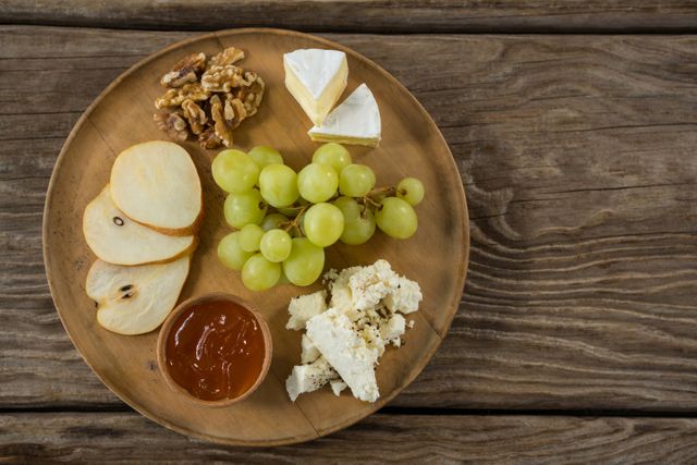 Close-up of cheese with grapes, apple slices, walnuts and sauce on wooden plate