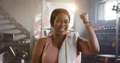 Mid-adult african american woman celebrating workout victory in industrial gym showing smartwatch