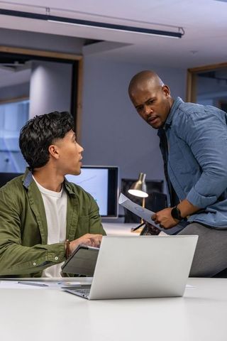 Diverse colleagues collaborating over laptop and documents in modern open office