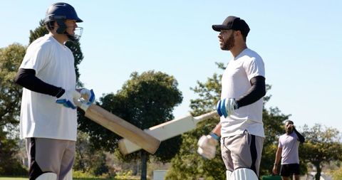 Cricket teammates tapping bats and bumping fists while walking off pitch on sunny park field