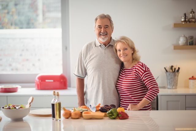 Portrait of smiling senior couple standing together in kitchen at home