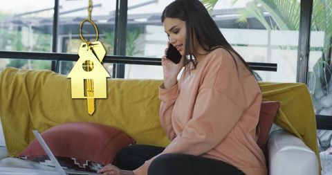 Woman using laptop at home with overlay of gold house key