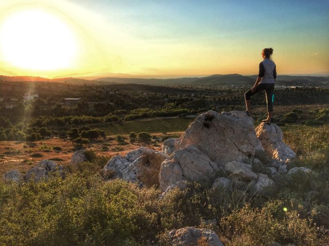 Person standing on rocks gazing at beautiful landscape during sunset. Perfect for themes related to exploring, adventure, nature appreciation, travel destinations, scenic outdoors, and mindfulness. Ideal for websites, blogs, social media posts, and promotional materials focusing on travel and outdoor activities.