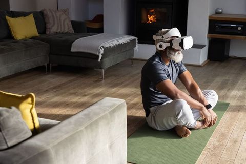 Senior african american man wearing vr headset on yoga mat near fireplace