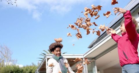 Happy Mother and Son Playing with Leaves in Autumn Garden