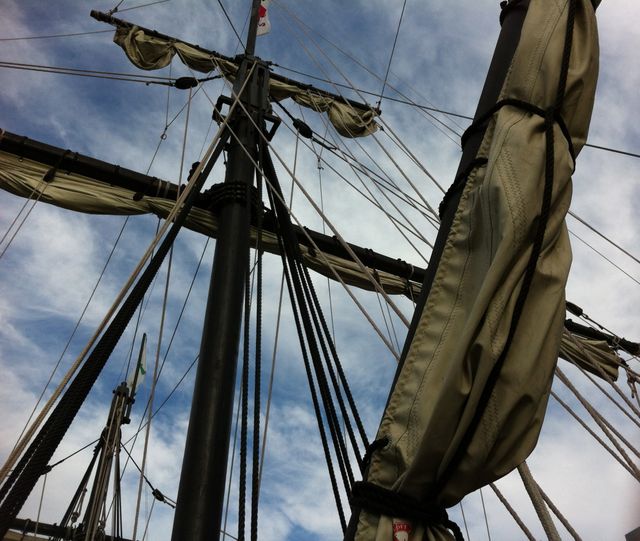 Detailed view of ship masts and rigging under a cloudy sky. Perfect for use in nautical themed projects, maritime history publications, or travel and adventure content related to sailing.
