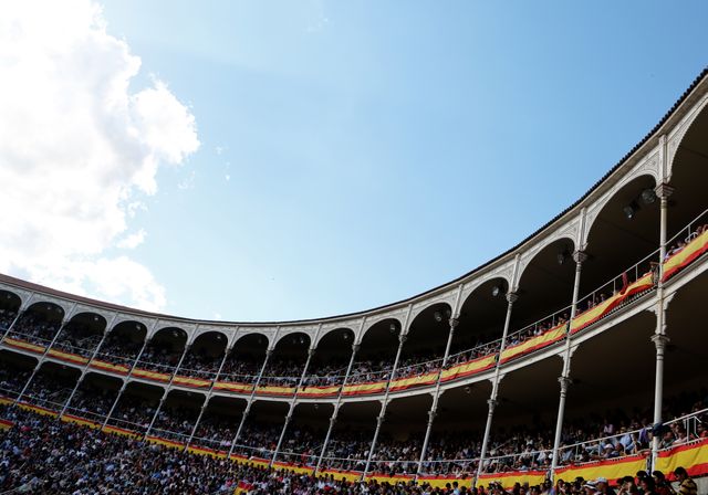 Rows of spectators seated in a large Roman-style amphitheater with columns and arches, with clear sky above. Ideal for use in themes related to Spanish culture, historical events, architecture, large public gatherings, and tourism in iconic venues.