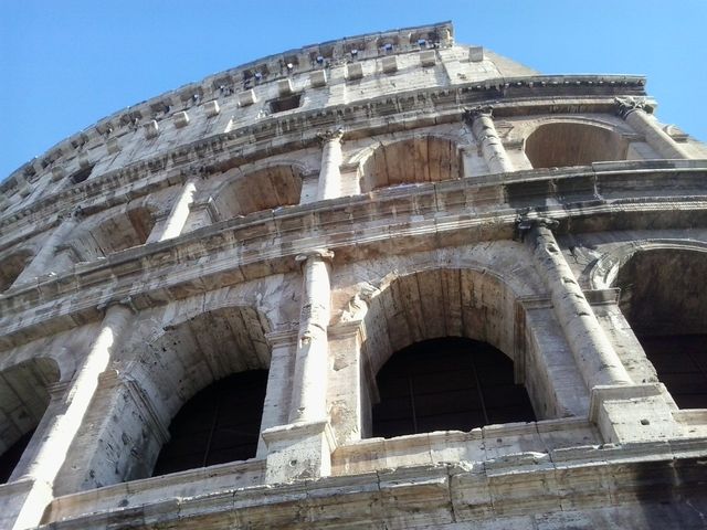Provides a close-up view of the Roman Colosseum highlighting its detailed architecture against a bright blue sky. Ideal for travel brochures, history presentations, educational materials, and promotional content about tourism in Rome.