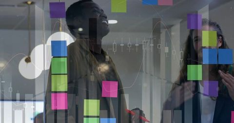 Colleagues collaborating at glass board with colorful sticky notes, marker, and data charts
