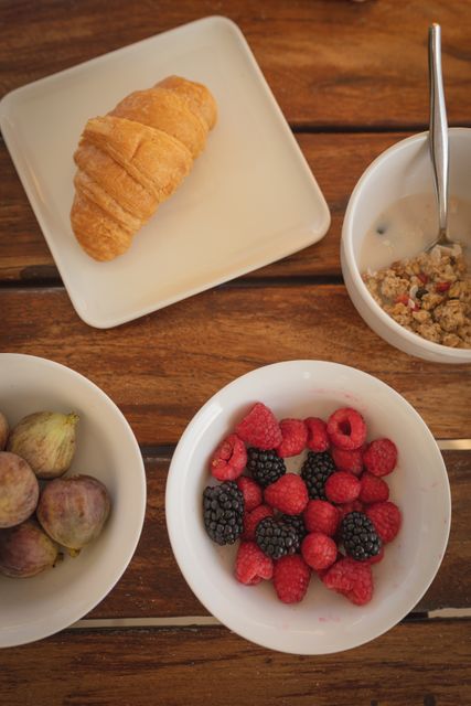 High angle close up of healthy breakfast with berries, figs, cereal in bowls and croissant on plate. Source of vitamin C during coronavirus Covid 19 pandemic.