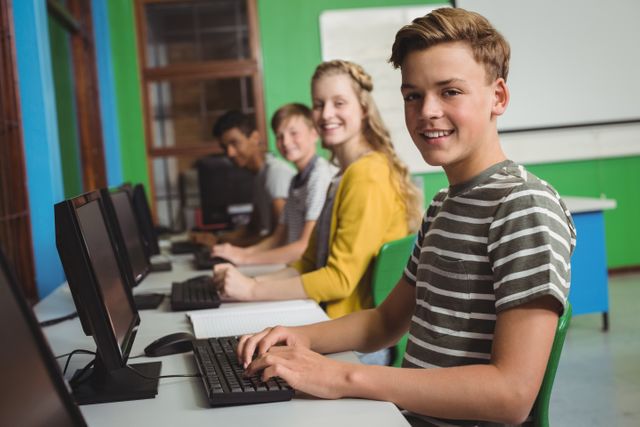 Group of students sitting in a row using desktop computers, smiling and engaged in their work. Suitable for content related to education, school activities, technology in classrooms, or teamwork in academic settings.