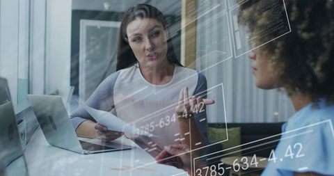 Businesswomen Discussing Strategy Over Documents and Laptop with Futuristic Data Overlay