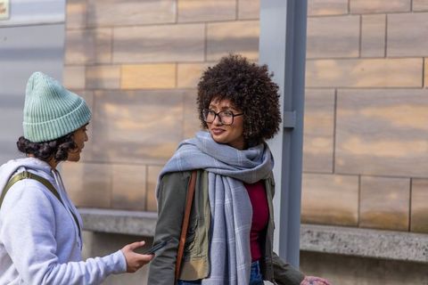 Urban friends walking and talking on sidewalk wearing scarves, jackets and backpacks