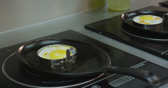 Close up of eggs being fried in two frying pans on kitchen stove in a restaurant. Busy chefs at work in commercial kitchen.