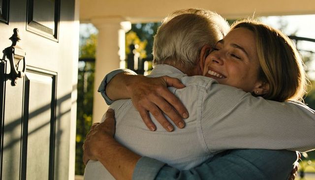 Daughter hugging father at front door on sunlit porch showing warm family reunion