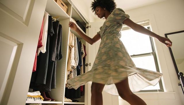 Woman twirling in light green floral midi dress in sunlit bedroom wardrobe near mirror