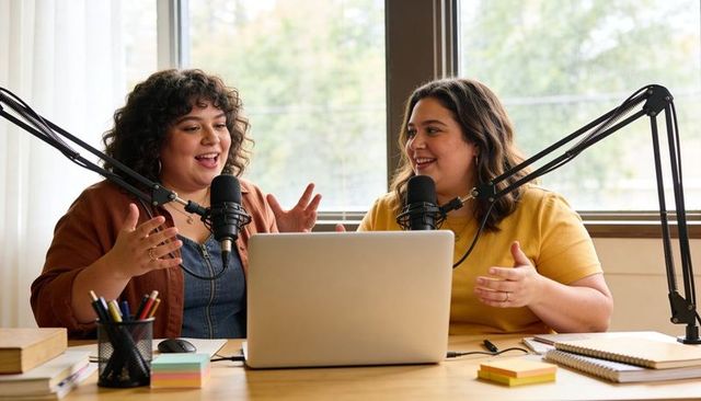 Recording podcast duo hosting lively conversation in cozy home studio with laptop
