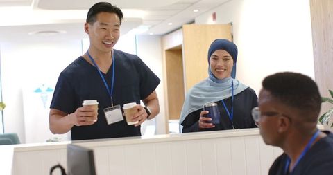 Smiling healthcare team holding coffee and chatting at modern clinic reception
