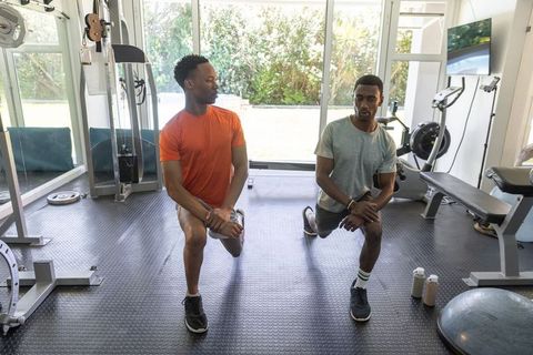 African american men performing forward lunges in sunlit home gym for partner fitness