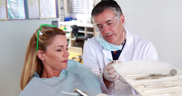 A middle-aged Caucasian dentist is providing care to a female patient in a dental clinic, with copy space. His focus and her relaxed demeanor suggest a professional and comfortable healthcare environment.
