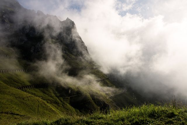 Misty mountain ridge featuring a steep path and vibrant greenery, enveloped in clouds. Ideal for conveying themes of adventure, exploration, and natural beauty. Perfect for travel agencies, outdoor magazines, trekking gear advertisements, and nature explorer blogs.