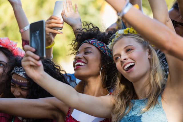 Women enjoying a music festival, capturing the moment with a selfie. Ideal for use in social media, festival promotions, lifestyle blogs, and advertisements focusing on youth culture, friendship, and outdoor events.
