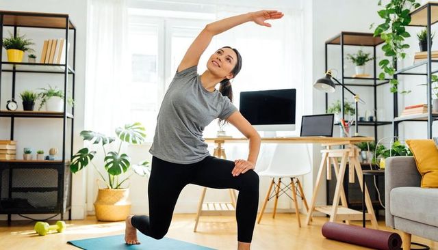 Young woman stretching on yoga mat in bright home office during remote work workout routine