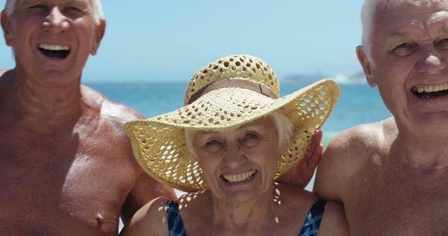 Group of cheerful senior friends enjoying a day at the beach under bright sunlight, posing happily. Perfect for travel, senior lifestyle, retirement community promotions, or elderly wellness campaigns.