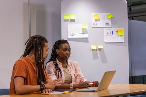 African american colleagues discussing strategy at laptop with charts and sticky notes