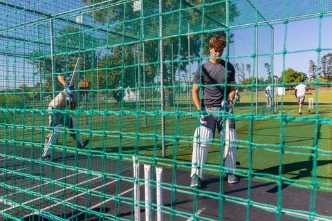 Cricket batsmen practicing in outdoor nets on sunny field with pads and gloves