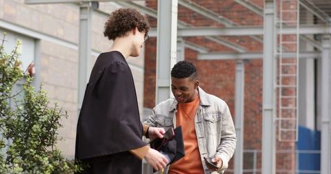 Graduation celebration: diverse friends in gown and mortarboard checking phone outdoors