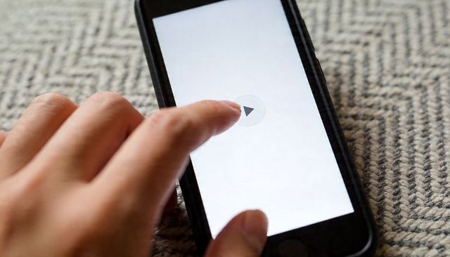 Finger Tapping Play Button on Smartphone Screen over Textured Woven Rug Closeup