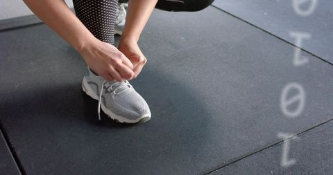 Close-up athlete tying running shoe on gym rubber tiles preparing for training session