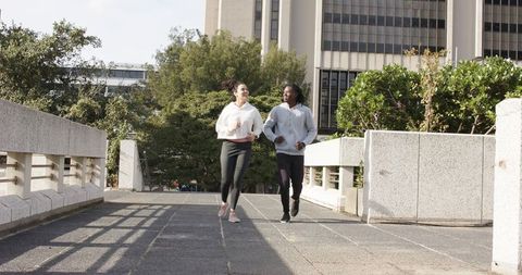 Diverse friends jogging together on urban pedestrian bridge in morning sunlight