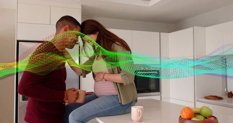 Expectant couple sharing tender moment in modern kitchen with colorful digital connection