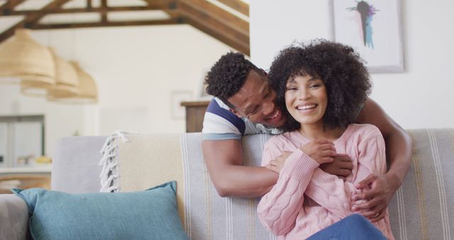 Happy couple sitting on a comfortable couch in a bright living room. Ideal for use in ads promoting home decor, lifestyle blogs, social media posts on relationships, or articles about family bonding and joy at home.