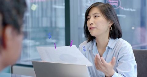 Korean woman presenting business strategy with laptop and documents in modern meeting room