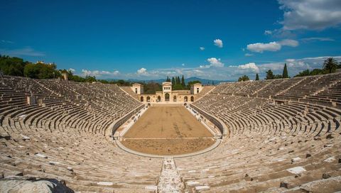 Sunlit ancient amphitheatre with curved stone tiers and sandy arena, roman ruins landscape