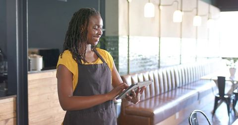 African Female Barista Using Tablet and Smiling in Modern Coffeehouse Interior