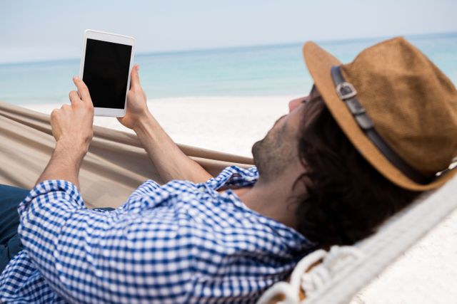 Man using tablet computer while lying in hammock at beach