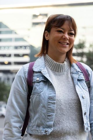 Smiling woman in denim jacket and gray sweater with purple backpack on city street