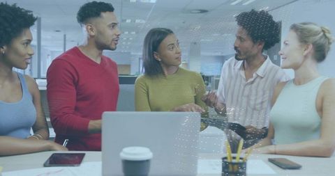 Diverse team collaborating around laptop and tablet in modern open office brainstorming