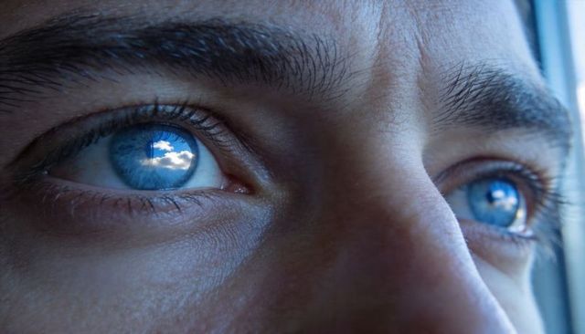 Man gazing with blue eyes reflecting sky and window, intimate close-up portrait